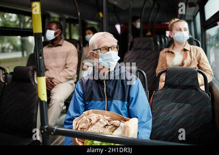 Ritratto di uomo anziano con maschera in autobus mentre si viaggia con i mezzi pubblici in città, spazio copia Foto Stock