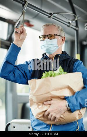 Ritratto verticale dell'uomo anziano che indossa la maschera in autobus mentre viaggia con i mezzi pubblici e tiene la ringhiera Foto Stock