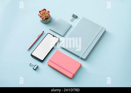 I colori puri a tema blu e rosa per ufficio stano ancora vita con notebook, smartphone, diario o diario, appunti, penna e fiore in una disposizione diagonale Foto Stock