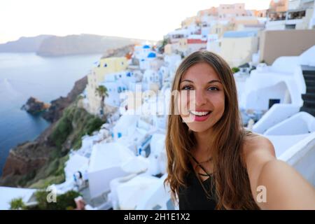 Autoritratto di ragazza sorridente nel villaggio di Oia, Santorini, Grecia. Felice ragazza turistica scattando foto selfie durante le vacanze estive a Santorini famosa E. Foto Stock