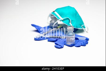 Due siringhe sopra i guanti blu per uso medico con due flaconcini di vaccino Covid-19 Test e una maschera per respiratore. Foto Stock