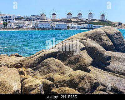 Mykonos mulini a vento in fila sullo sfondo, rocce sulla spiaggia in primo piano, Grecia Foto Stock