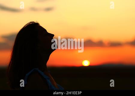 Ritratto con vista laterale di una silhouette retroilluminata di una donna che respira aria fresca all'alba Foto Stock