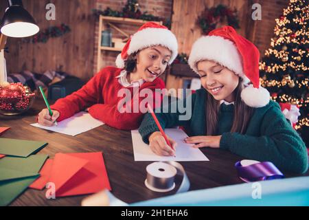 Ritratto di due fratelli allegri attraenti che scrivono le lettere sogno desiderabili lista dei regali che genera l'artigianato alla sede del loft del mattone all'interno Foto Stock