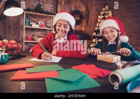 Ritratto di due fratelli allegri attraenti che preparano le lettere di scrittura del tempo della vigilia desiderano i regali di imballaggio del sogno alla sede interna del loft del mattone Foto Stock