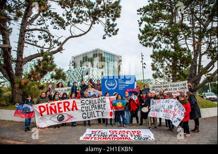 I manifestanti hanno striscioni che esprimono le loro opinioni durante la dimostrazione.i cileni sono visti posare con bandiere e striscioni contro il presidente cileno di fronte all'edificio ICC. In occasione del secondo anniversario dell'epidemia sociale cilena, le persone cilene che vivono in diverse città europee si sono riunite di fronte al Tribunale penale internazionale (CPI) per chiedere il processo internazionale di Piñera per i suoi crimini contro l'umanità. Sono stati accompagnati dall'osservatore dell'Unione europea Maria Teresa Mola Sainz, che ha espresso preoccupazione per le sistematiche violazioni dei diritti umani commesse da Chilea Foto Stock