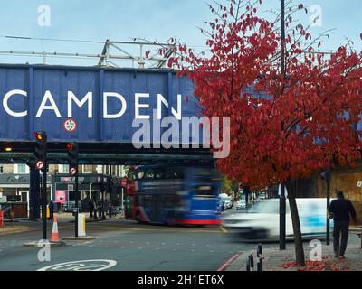 Londra, Regno Unito; ottobre 2021 - le foglie ardenti di un ciliegio contro l'emblematico cartello del ponte ferroviario Camden, con la vita cittadina sfocata sotto. Foto Stock