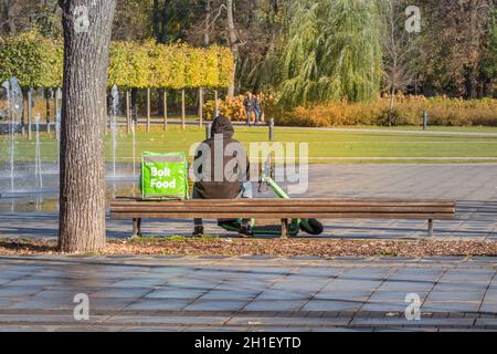 Vilnius, Lituania - 16 ottobre 2021: Consegna di cibo Bolt in città. Il corriere seduto sul banco e in attesa di consegnare il cibo a casa o. Foto Stock