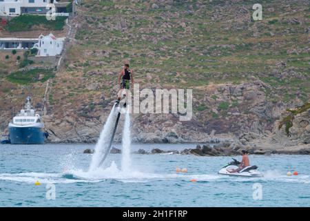 MYKONOS, GRECIA - 29 MAGGIO 2019: Uomo che vola flyboard su un Flyboard - dispositivo di hydroflighting che fornisce propulsione per guidare il Flyboard inventato Foto Stock