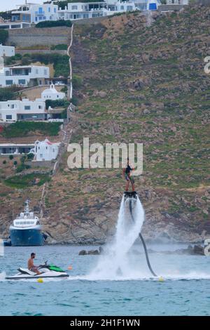MYKONOS, GRECIA - 29 MAGGIO 2019: Uomo che vola flyboard su un Flyboard - dispositivo di hydroflighting che fornisce propulsione per guidare il Flyboard inventato Foto Stock