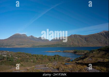 Vista sulla foresta e Loch Torridon fino alle montagne Beinn Alligin e Liathach in una giornata di sole. Cielo blu e nuvola di luce con getto d'acqua. Nessuna gente. Foto Stock