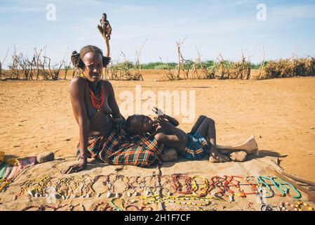 Omorate, Valle dell'Omo, Etiopia - 11 maggio 2019: Donna della tribù africana Dasanesh con bambino che offre souvenir fatti a mano. Daasanach sono etnie Cushitiche Foto Stock