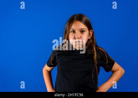 La bambina puffed fuori le sue guance isolato su sfondo blu studio. Concetto gestuale Foto Stock
