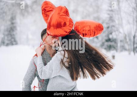 Coppia amorevole coccole nella foresta invernale tenendo palloncini a forma di cuore Foto Stock