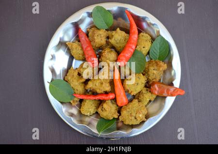 Primo piano il mazzetto giallo marrone bengala grammo fritto cibo con peperoncino rosso e menta verde nel piatto Foto Stock