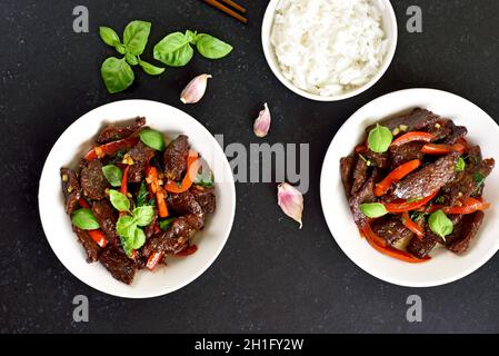 Frittura di manzo thailandese con pepe e basilico in una ciotola su sfondo scuro. Vista dall'alto, piatto Foto Stock