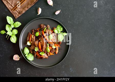 Frittura di manzo thailandese con pepe e basilico su sfondo scuro con spazio copia. Vista dall'alto, piatto Foto Stock