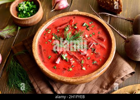 Gustosa zuppa di barbabietole con panna acida e verdure in ciotola, borscht su tavolo di legno, vista ravvicinata Foto Stock