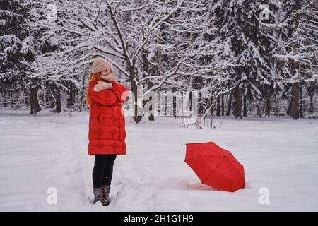 Una donna sorridente si avvolge in abiti che si riscaldano in una foresta invernale con alberi nella neve Foto Stock