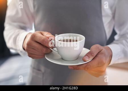 Un uomo tiene una tazza bianca con una bevanda calda all'aperto. Mano di un uomo che tiene una tazza di caffè. Primo piano, layout immagine, posizione per copiare il testo. Foto di alta qualità Foto Stock