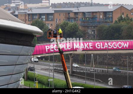 Glasgow, Scozia, Regno Unito. 18 Ott 2021. Glasgow continua a prepararsi per la COP26. Nella foto: La gente fa il logo Glasgow sulla passerella pedonale sopra la Clydeside Expressway. La Clydeside Expressway sarà chiusa tra il 23 ottobre e il 14 novembre credito: Kay Roxby/Alamy Live News Foto Stock