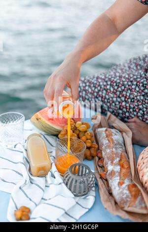 La mano della donna versa il succo in un bicchiere in un picnic vicino al mare Foto Stock