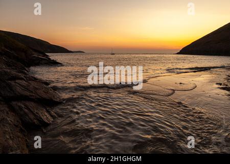 Uno yacht soleggiato si trova al largo di Mwnt Beach, mentre il sole tramonta in una tranquilla serata estiva Foto Stock