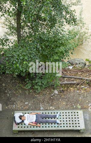 Graz, Austria. Agosto 2020. Un giovane stanco riposa su una panchina sul lungofiume di Mur Foto Stock