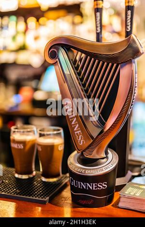 Dublino, Irlanda, agosto 2018 fuoco selettivo sul rubinetto di Guinness con le pinte offuscate della birra schiumosa e della parete delle bottiglie. Guinness è l'iconica birra irlandese Foto Stock