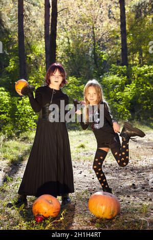 Due sorelle felici nella foresta di Halloween. Divertenti bambini in costumi di carnevale all'aperto a Halloween trick o delizia. Buon Halloween! Foto Stock