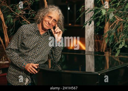 ritratto di maturo musicista maschile di 65 anni, artista, si appoggiò su una mano grande pianoforte, sorrise e pensò. Foto Stock