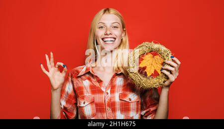 Donna felice con la corona d'autunno mostra segno ok. Corona decorativa del Ringraziamento con foglia di acero. Umore autunnale. Foto Stock