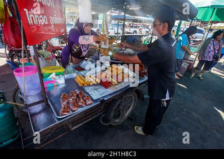 Khao Lak, Tailandia - 22 Febbraio 2016: Sconosciuto uomo acquisto prima colazione dal commerciante locale con il suo stallo mobile sul mercato mattutino. Cucina tailandese è ren Foto Stock