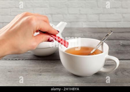 Dettagli sulla donna mano versando zucchero dal pacchetto di piccole dimensioni nella tazza di tè caldo. Foto Stock