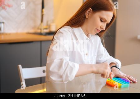 Vista laterale di una giovane donna stressata che gioca con il giocattolo sensoriale Fidget per alleviare lo stress in modo semplice per essere in calma e armonia a casa. Foto Stock