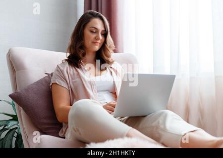 La donna usa un notebook a casa. Giovane 30s calma caucasica donna brunette con bei capelli in abiti casual che lavorano su laptop o fare shopping online a. Foto Stock