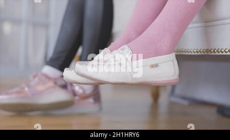 Le gambe dei bambini oscillano. Azione. Primo piano delle gambe dei bambini appese al lussuoso divano. I bambini stanno aspettando seduti sul divano che oscura le gambe. Foto Stock