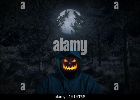Ritratto di un uomo con una zucca invece di una testa in piedi nella foresta oscura con luce lunare. Horror Halloween concetto. Foto Stock