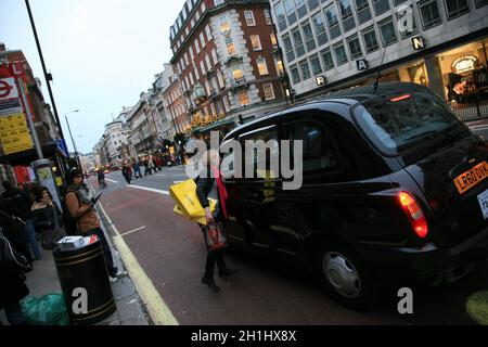 Londra, Regno Unito - 13 novembre 2010: Taxi nella strada di Londra. Passeggero donna con borse per la spesa che chiede all'autista prima di salire a bordo. Le cabine nere sono il Foto Stock