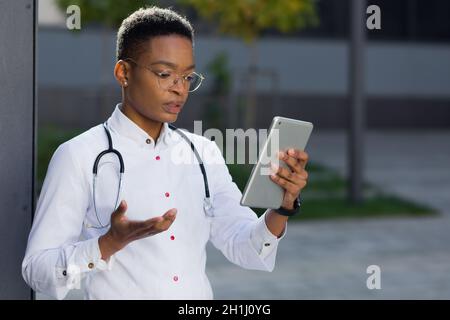 La dottoressa conduce una consultazione online tramite video link che tiene un tablet, vicino alla clinica, una conferenza a pranzo con il personale Foto Stock