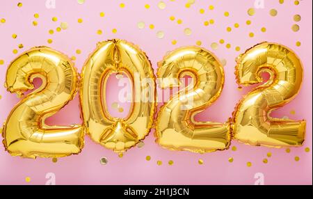 palloncini d'oro a 2022 anni con confetti su sfondo rosa. Felice anno nuovo 2022 lettere festa della vigilia. Buon concetto di Natale. Nastro lungo Foto Stock