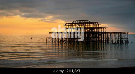 Il derelitto West Pier su un tramonto nuvoloso, Brighton, Inghilterra. Costruito nel 1866 e chiuso nel 1975, il molo è ancora classificato di grado i e un punto di riferimento ben noto. Gli uccelli si affollano alla struttura arrugginosa. Foto Stock