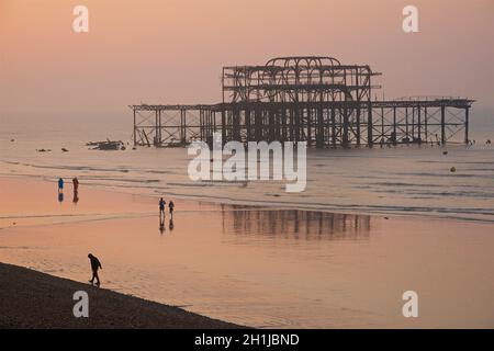 La forma silhouette delle rovine del vecchio West Pier in bassa marea in un crepuscolo rosa pre-alba giorno. . Brighton & Hove, Sussex, Inghilterra, Regno Unito. La gente gode di una passeggiata di mattina presto sulla sabbia. Foto Stock