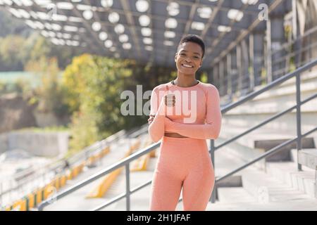 La giovane atleta femminile guarda la macchina fotografica e sorride, le trincee sportive ostinate e motivate incoraggiano lo sport e lo stile di vita attivo Foto Stock