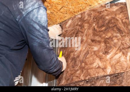 Riparazione della casa. L'operaio isola le pareti con lana minerale per ulteriore rivestimento con cartongesso. Isolamento termico e isolamento acustico dell'alloggiamento Foto Stock