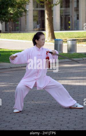 Una donna aggraziata di mezza età fa Tai Chi con una spada. Nel Flushing Meadows Corona Park a Queens, New York City. Foto Stock