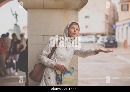 Bellissima femmina turistico con una mappa alla scoperta di una città straniera - Attesa per la pioggia per interrompere (SHALLOW DOF; dai toni di colore immagine) Foto Stock