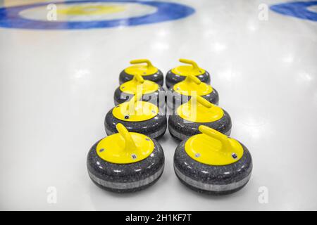 La pietra curling o roccia è fatta di granito con manici gialli giacciono sul ghiaccio, sullo sfondo un bersaglio circolare segnato sulla casa di ghiaccio Foto Stock