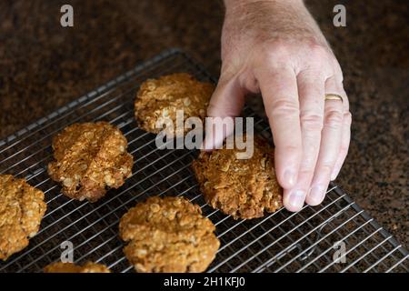 Maschio a mano che raccoglie il biscotto anzac dalla griglia di raffreddamento. Foto Stock