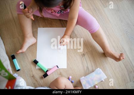 Paesaggio immagine di una bambina in abiti rosa seduta su un pavimento di legno e fare somme su un foglio di carta con coloratissimi textmarkers, e cotone ba Foto Stock
